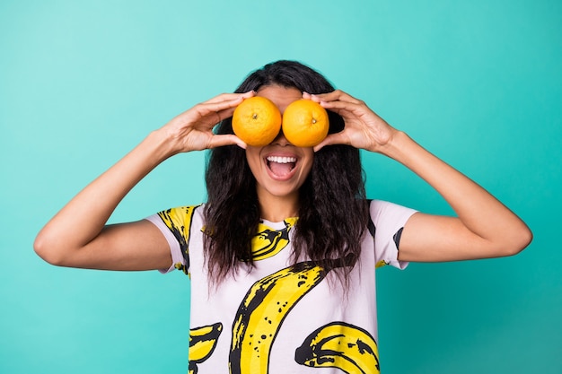 Foto de niña mantenga dos naranjas cerrar los ojos con la boca abierta llevar camiseta con estampado de plátano aislado de fondo de color turquesa