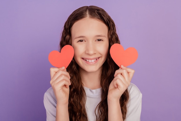 Foto de niña mostrar corazón de San Valentín de papel aislado sobre fondo púrpura