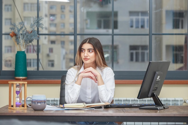 Foto de una niña sentada en el escritorio y juntó las manos.