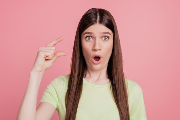 Foto de niña sorprendida conmocionada mostrar los dedos pequeña medida de tamaño diminuto aislado sobre fondo de color rosa