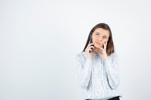 Foto de niña en suéter hablando con alguien por teléfono celular.