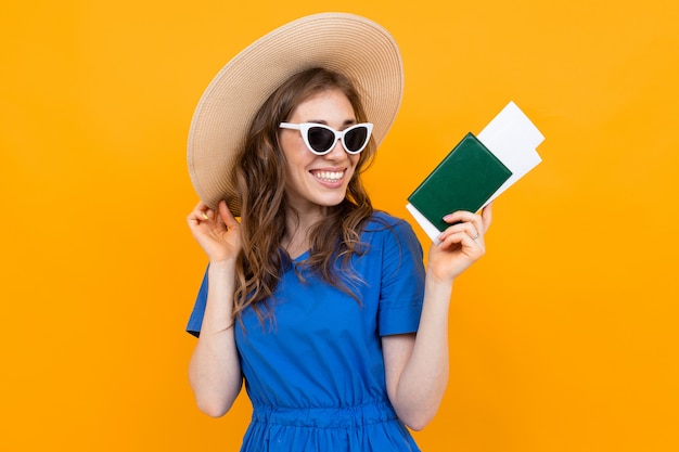 Foto de una niña turista con un boleto y un pasaporte en sus manos contra el fondo de una pared naranja