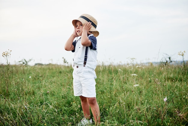 Foto de niño elegante al aire libre en la hierba verde alta en el campo.