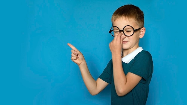 Foto foto de un niño feliz sonriente apuntando con su dedo hacia el lugar para copiar resaltado en un fondo simple regreso a la escuela niño divertido con gafas de la escuela primaria educación