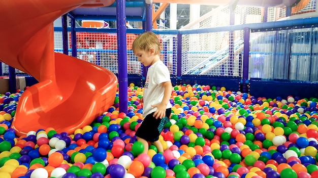 Foto de niño jugando en la piscina llena de bolas de plástico colroful. Niño divirtiéndose en el patio de recreo en el centro comercial