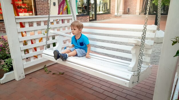 Foto de niño niño sentado en un banco de madera blanca en la vieja calle de la ciudad europea