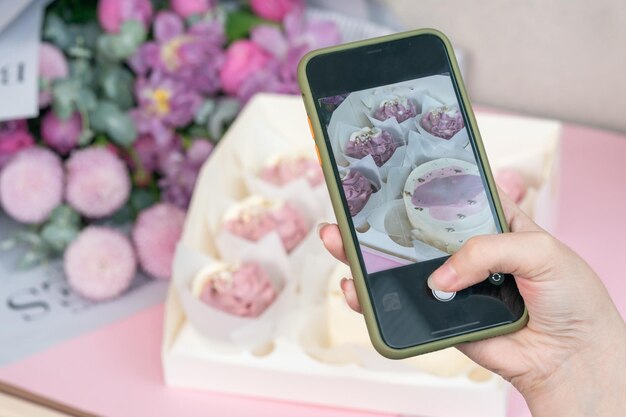 Foto no telefone de cupcakes frescos e lindas flores em uma mesa