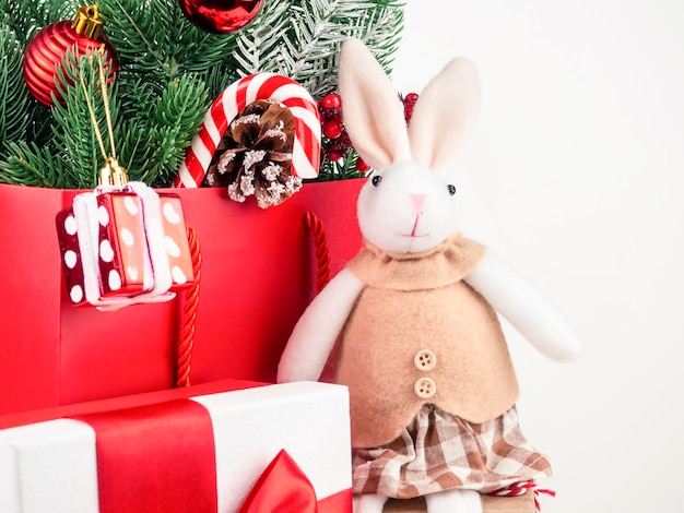 Foto de Nochevieja con una bolsa roja con ramas de abeto y regalos de Navidad con un conejo sentado en ella. La foto se puede usar para tarjetas, calendarios, volantes. Primer plano.