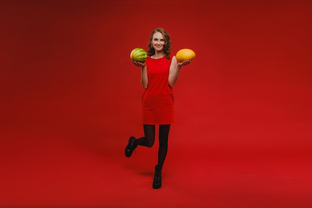 Foto de novia linda positiva alegre ondulada sonriendo y con melones aislados sobre pared roja vívida