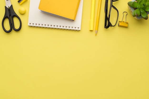 Foto oben von Notizbuch, Stift, Brille, Pflanze, Schere, Spitzer und Büroklammern, isoliert auf gelbem Hintergrund