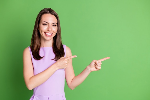 Foto optimista chica guapa dama radiante sonrisa punto doble dedo índice espacio vacío consejo producto servicio clínica dental seguir ventas vestido camiseta púrpura aislado fondo de color verde