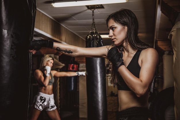 Foto oscura de una joven mujer bonita en un gimnasio oscuro, que tiene un entrenamiento con saco de boxeo.