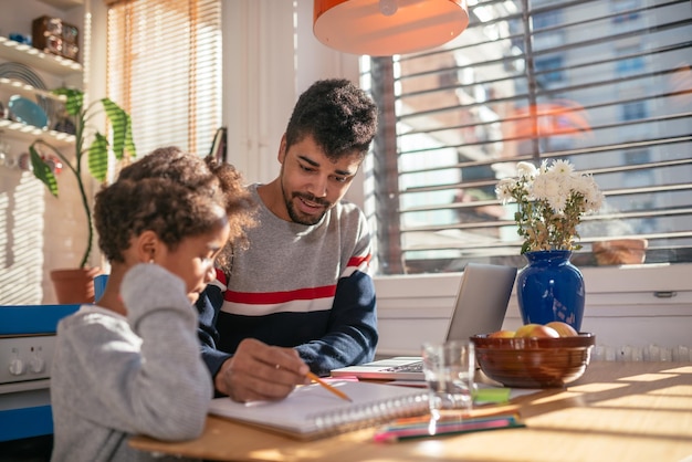 Foto de un padre joven que disfruta dibujar con su hijita en casa