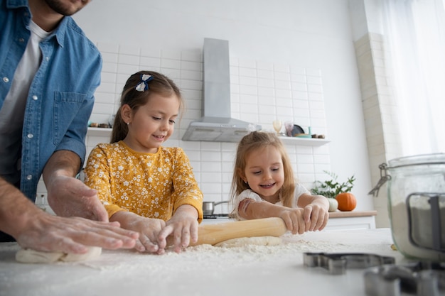 Foto de un padre sonriente y sus hijas horneando en la cocina y divirtiéndose.