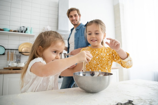 Foto de un padre sonriente y sus hijas horneando en la cocina y divirtiéndose.