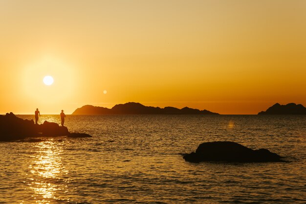 Foto de paisaje de dos pescadores bajo la puesta de sol