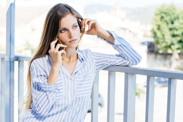 Foto de paisaje de una mujer joven con una camisa a rayas blancas y azules hablando por teléfono