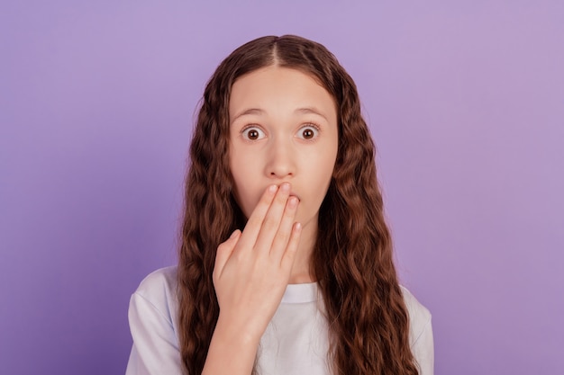 Foto de la palma de la niña de la escuela joven cubriendo los labios de la boca aislado sobre fondo violeta