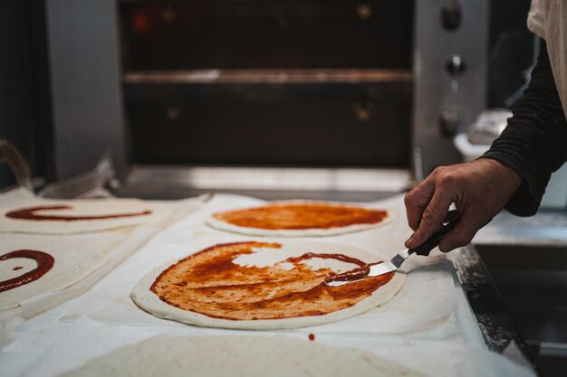 Una foto de un panadero esparciendo salsa de tomate sobre la masa de pizza antes de meterla en el horno