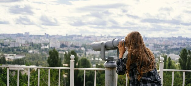 Foto de pancarta de una mujer rubia mirando a la ciudad a través de unos grandes binoculares