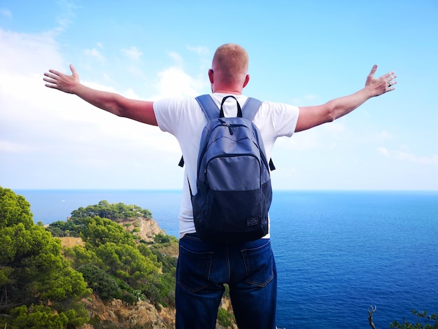 Foto panorâmica de um homem feliz com os braços estendidos que conquistou o pico da vida com uma bela vista do mar e da costa rochosa O conceito de viagem e liberdade