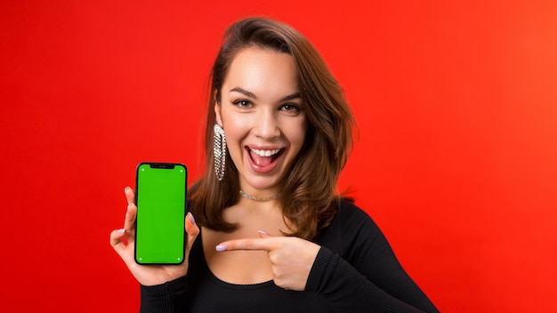 Foto foto panorâmica de uma jovem com um telefone celular com chroma key em um fundo vermelho