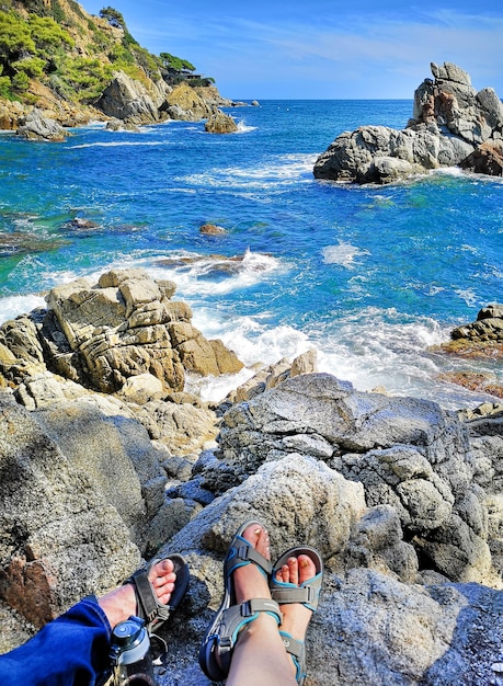 Foto panorâmica do litoral rochoso com os pés de turistas em sandálias mulheres e homens O conceito de caminhadas de pessoas comuns ao longo da costa