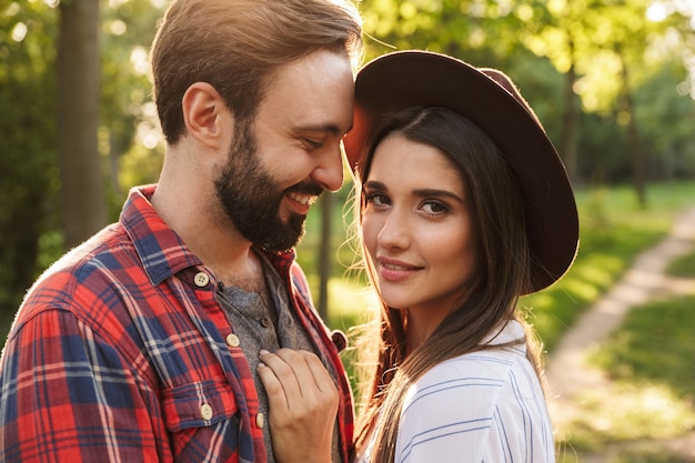 Foto de una pareja amorosa joven romántica complacida sonriente caminando al aire libre en un bosque de parque natural verde besos.