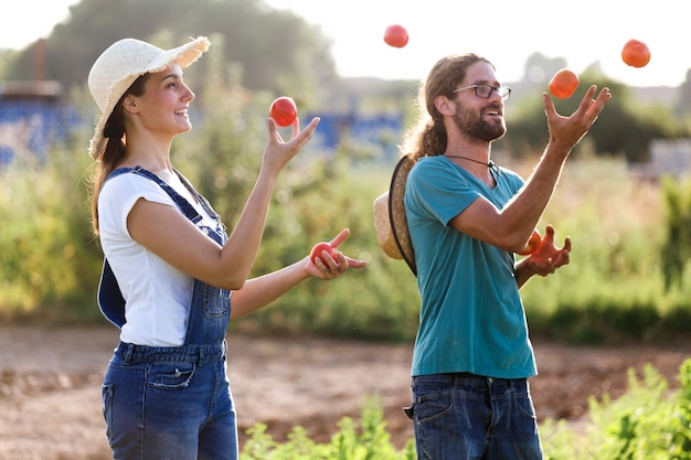 Foto de pareja divertida horticultor jugando y haciendo malabares con tomates frescos en el jardín.