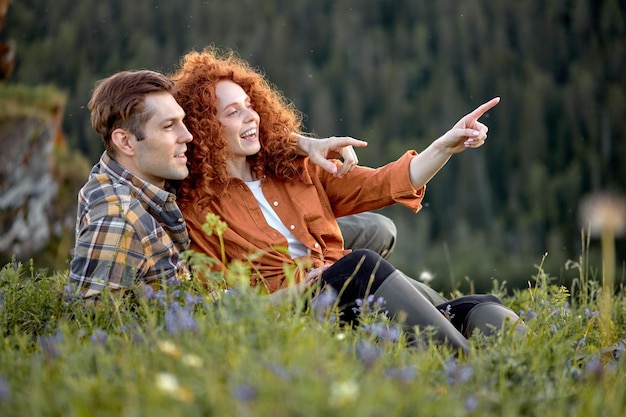 Una foto de una pareja joven y romántica sentada en un prado en las montañas.