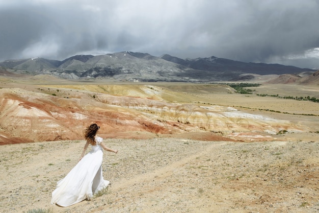 Foto foto de la parte de atrás una mujer-novia vestida de novia camina con confianza por las montañas del desierto con una hermosa vista. concepto de viaje de luna de miel