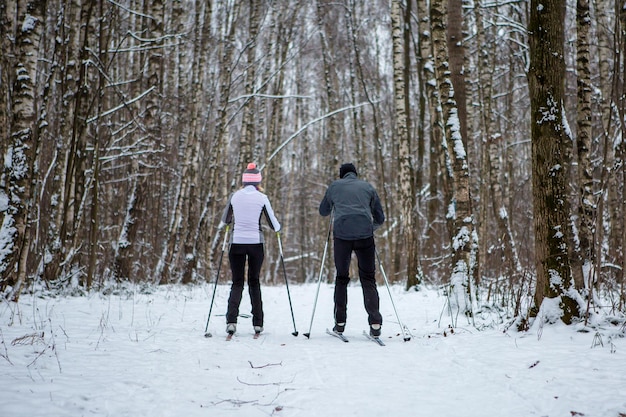 Foto de la parte trasera de una mujer y un hombre deportistas esquiando en un bosque invernal