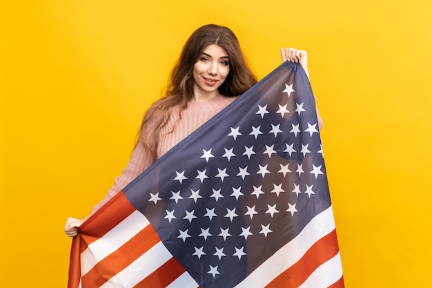 Esta foto patriótica muestra a una mujer joven que sostiene con orgullo la bandera estadounidense contra un fondo amarillo vibrante.