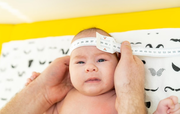 Foto de un pediatra examinando al bebé recién nacido Doctor usando cinta métrica comprobando el tamaño de la cabeza del bebé Primer plano