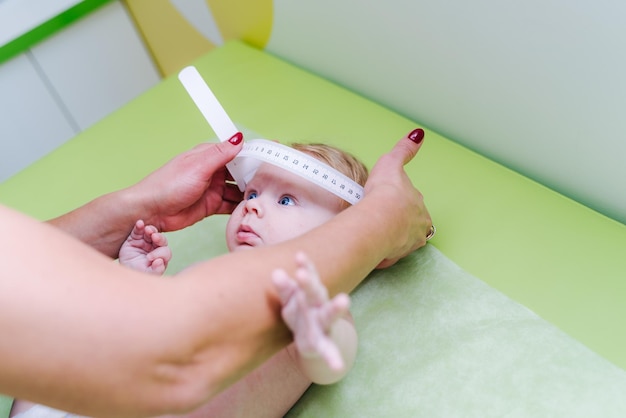 Foto de un pediatra que examina al bebé recién nacido Doctor usando cinta métrica para comprobar el tamaño de la cabeza del bebé Primer plano