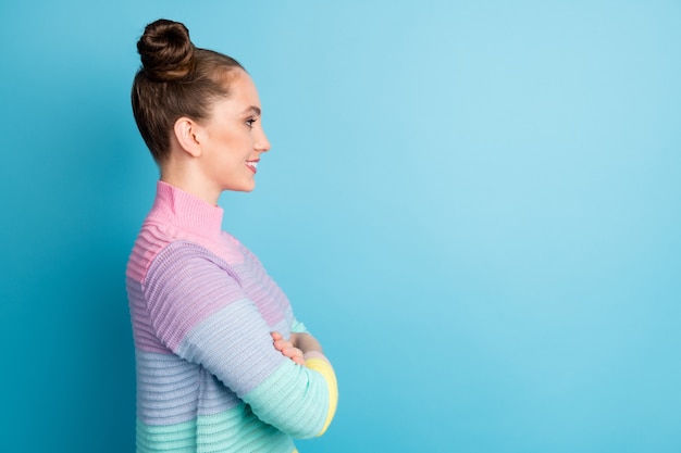 Foto de perfil de dama atractiva dos bollos de buen humor brazos cruzados mirar lateral espacio vacío concentrado emoción positiva desgaste casual cálido suéter a rayas aislado fondo de color azul