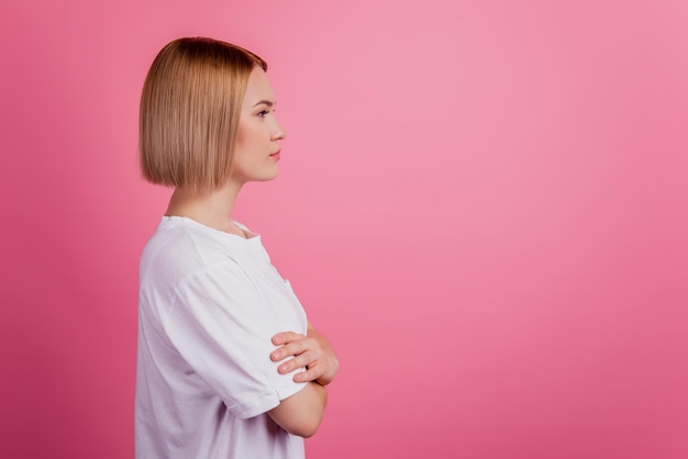 Foto de perfil de dama segura de sí misma mira el espacio vacío con los brazos cruzados y la camiseta blanca aislada sobre fondo rosa