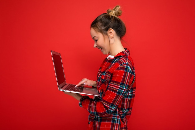 Foto de perfil lateral de bastante joven sosteniendo netbook mirando la pantalla escribiendo en el teclado