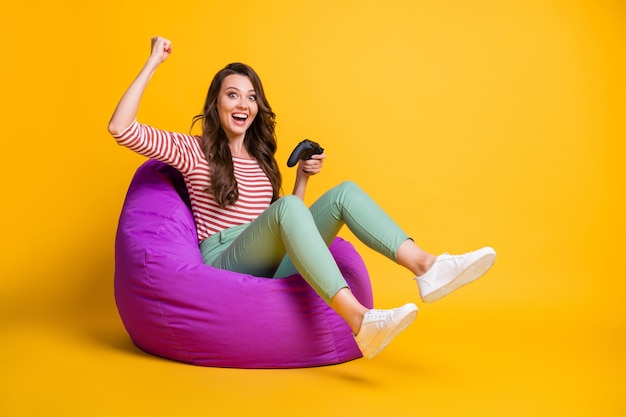 Foto de perfil lateral de tamaño de cuerpo completo de niña con consola celebrando la victoria aislada sobre fondo de color amarillo vivo con espacio vacío