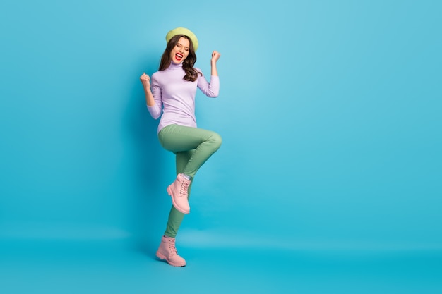 Foto de perfil de longitud completa de la hermosa dama turística a pie de la calle celebrando la visita a la ciudad de ensueño, desgaste del país, boina verde, púrpura, pantalones, zapatos, aislado, pared de color azul