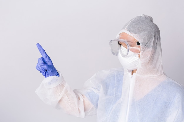 Foto de perfil de un médico en puntos de equipo de protección con el dedo índice hacia el lado sobre fondo blanco aislado