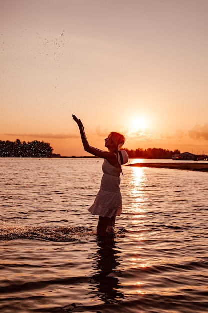 Foto de perfil de mujer salpicaduras de agua silueta de hermosa rubia delgada feliz en un vestido de verano ...