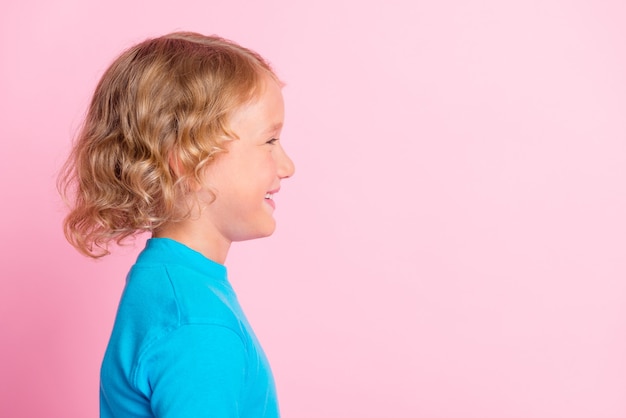 Foto de perfil de niño alegre mirar espacio vacío usar cuello alto azul aislado fondo de color rosa pastel