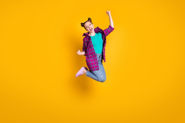 Foto de perfil de tamaño completo de una dama adolescente emocionada bastante loca saltar arriba competencia de buen humor ganando levantar puños usar camisa a cuadros casual zapatillas de deporte jeans zapatos aislado fondo de color amarillo