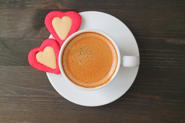 Foto plana de café exprés con dos galletas en forma de corazón sobre una mesa de madera de color marrón oscuro