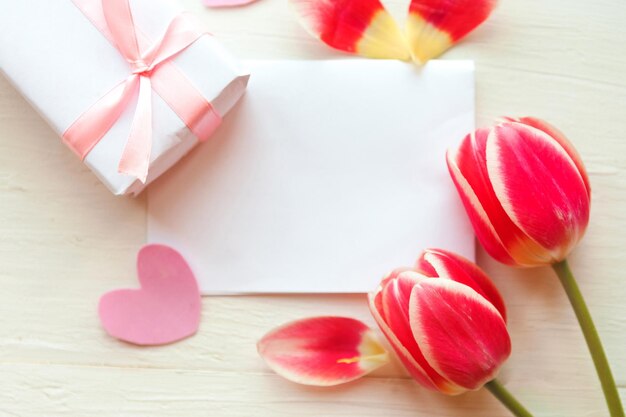 Foto plana con caja de regalos y tulipanes rojos en fondo de madera hermosa tarjeta de felicitación para el Día de las Madres, el Día de la Mujer o el Día de San Valentín