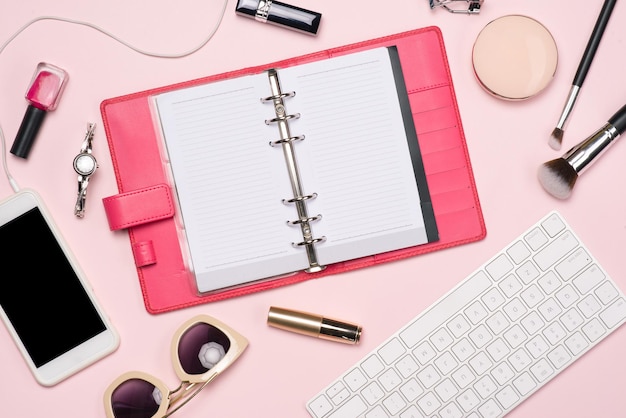 Foto plana creativa del espacio de trabajo con cosméticos, café, teléfono inteligente, gafas, rímel, brillo con espacio de copia sobre fondo rosa