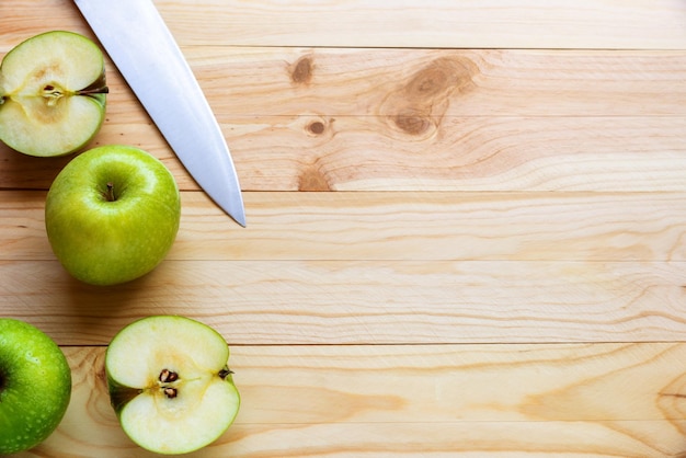 Foto plana leiga de algumas maçãs verdes, uma das quais cortada com uma faca sobre um fundo de madeira natural