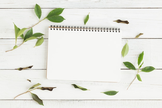 Foto plana leiga de caderno branco em branco e folha verde na mesa de madeira branca