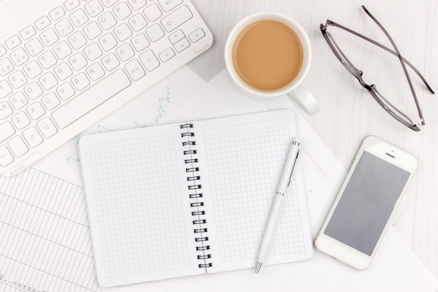 Foto plana de la posición del escritorio de oficina blanco con el ordenador portátil, el smartphone, las lentes, el cuaderno y la pluma con el fondo del espacio de la copia. Bosquejo